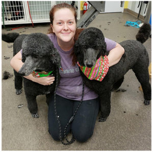 woman hugging two black poodles